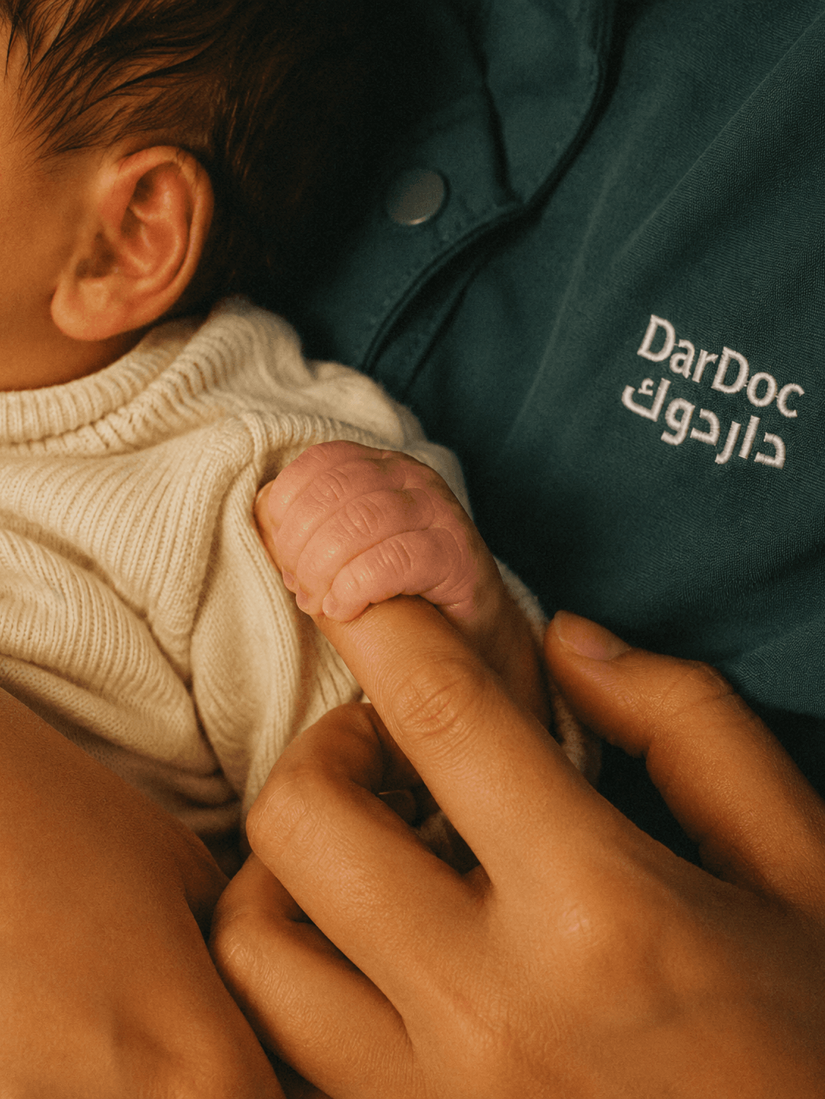 Newborn holding a DarDoc caregiver's finger